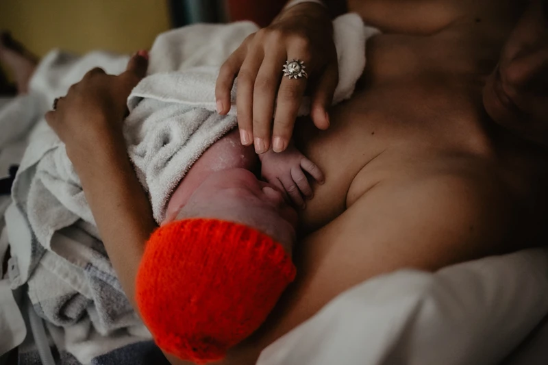 Newborn baby in a hat on mother's chest 