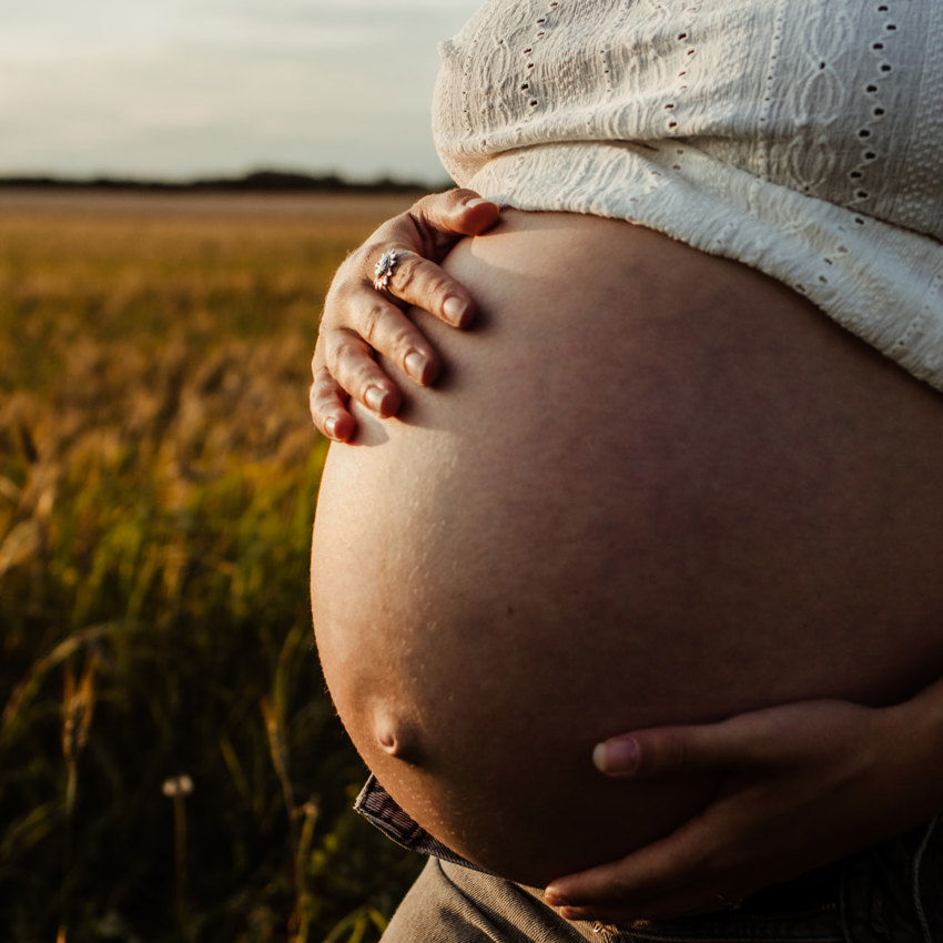 Pregnant woman holding bump in a field at sunset